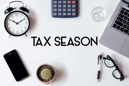 Tax Season words written on white table with clock, smartphone, calculator, pen, cactus, glass and laptopの写真素材