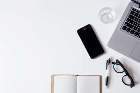 White office desk table with laptop, smartphone, notebook, and glass. Top view with copy space, flat lay.の写真素材