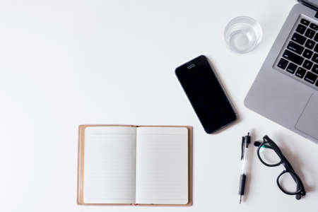 White office desk table with laptop, smartphone, notebook, and glass. Top view with copy space, flat lay.の写真素材