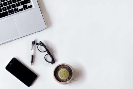 White office desk table with laptop, cactus, smartphone, and glass. Top view with copy space, flat lay.の写真素材