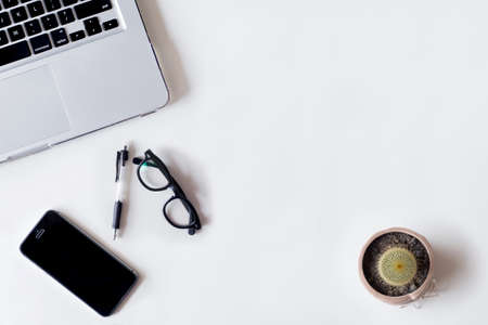 White office desk table with laptop, cactus, smartphone, and glass. Top view with copy space, flat lay.の写真素材