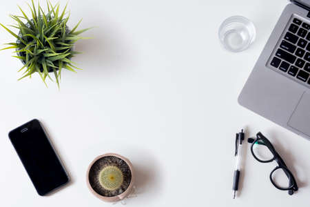 White office desk table with laptop, smartphone, and glass. Top view with copy space, flat lay.の写真素材