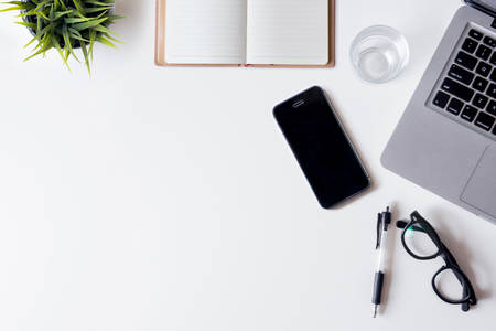 White office desk table with laptop, smartphone, notebook, and glass. Top view with copy space, flat lay.の写真素材
