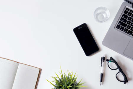White office desk table with laptop, smartphone, notebook, and glass. Top view with copy space, flat lay.の写真素材
