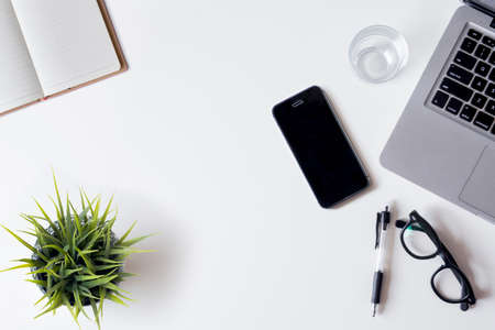 White office desk table with laptop, smartphone, notebook, and glass. Top view with copy space, flat lay.の写真素材