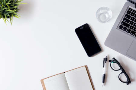 White office desk table with laptop, smartphone, notebook, and glass. Top view with copy space, flat lay.の写真素材
