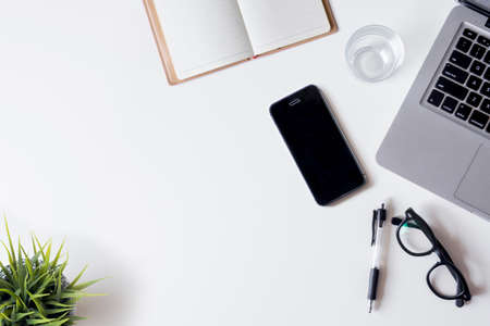 White office desk table with laptop, smartphone, notebook, and glass. Top view with copy space, flat lay.の写真素材