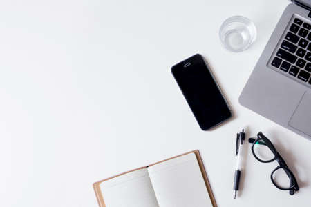 White office desk table with laptop, smartphone, notebook, and glass. Top view with copy space, flat lay.の写真素材