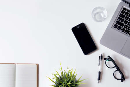 White office desk table with laptop, smartphone, notebook, and glass. Top view with copy space, flat lay.の写真素材