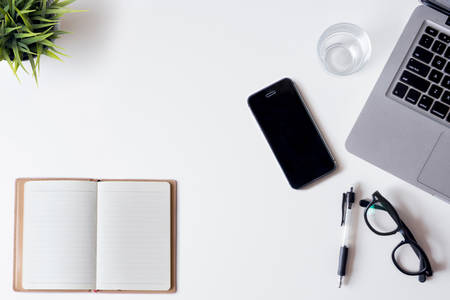 White office desk table with laptop, smartphone, notebook, and glass. Top view with copy space, flat lay.の写真素材