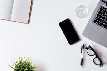 White office desk table with laptop, smartphone, notebook, and glass. Top view with copy space, flat lay.の写真素材