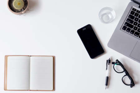 White office desk table with laptop, smartphone, notebook, and glass. Top view with copy space, flat lay.の写真素材