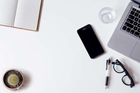White office desk table with laptop, smartphone, notebook, and glass. Top view with copy space, flat lay.の写真素材