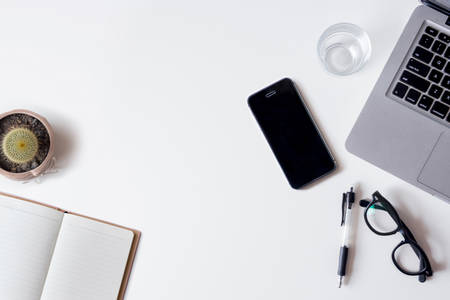 White office desk table with laptop, smartphone, notebook, and glass. Top view with copy space, flat lay.の写真素材