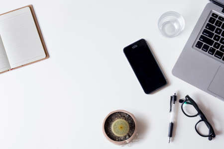 White office desk table with laptop, smartphone, notebook, and glass. Top view with copy space, flat lay.の写真素材
