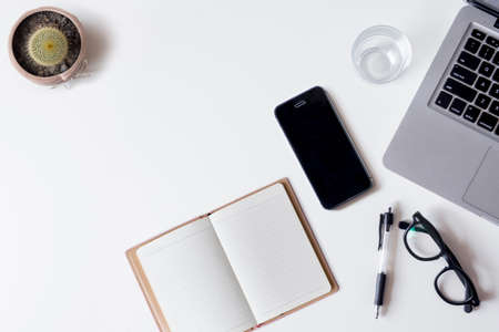 White office desk table with laptop, smartphone, notebook, and glass. Top view with copy space, flat lay.の写真素材