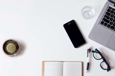 White office desk table with laptop, smartphone, notebook, and glass. Top view with copy space, flat lay.の写真素材