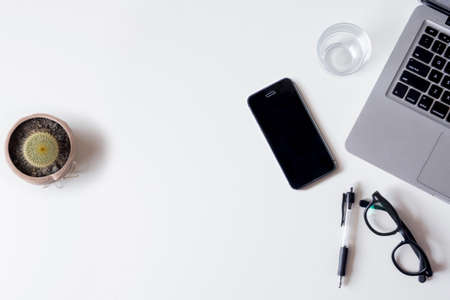 White office desk table with laptop, smartphone, cactus and glass. Top view with copy space, flat lay.の写真素材