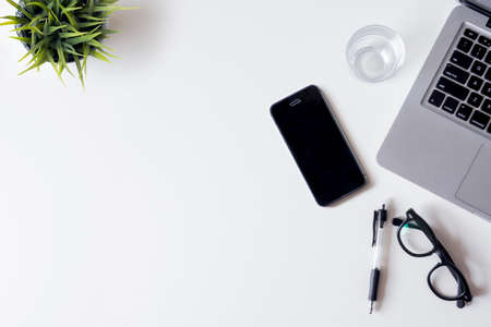 White office desk table with laptop, smartphone, plant and glass. Top view with copy space, flat lay.の写真素材