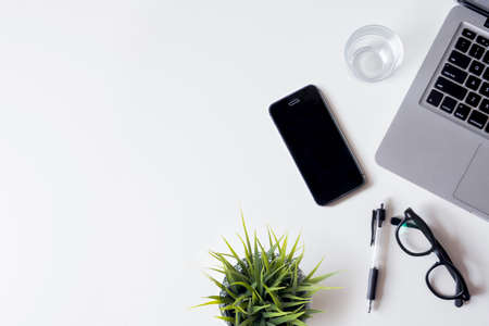 White office desk table with laptop, smartphone, plant and glass. Top view with copy space, flat lay.の写真素材