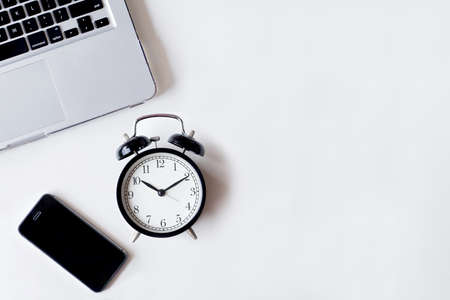 White office desk table with laptop, smartphone, and alarm clock. Top view with copy space, flat lay.の写真素材
