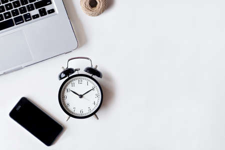 White office desk table with laptop, smartphone, and alarm clock. Top view with copy space, flat lay.の写真素材