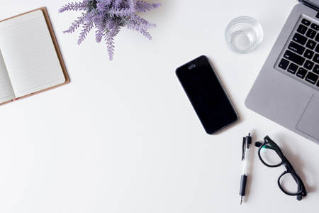White office desk table with laptop, smartphone, notebook, lavender, and glass. Top view with copy space, flat lay.の写真素材