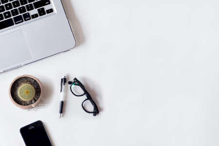 White office desk table with laptop, cactus, smartphone, pen, and glass. Top view with copy space, flat lay.の写真素材