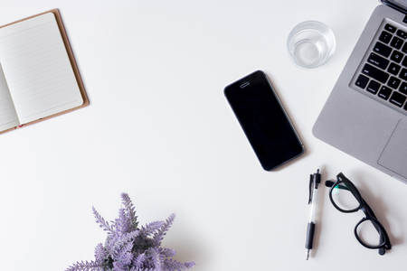 White office desk table with laptop, smartphone, notebook, lavender, and glass. Top view with copy space, flat lay.の写真素材