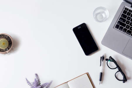 White office desk table with laptop, smartphone, notebook, cactus, and glass. Top view with copy space, flat lay.の写真素材