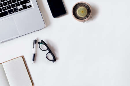 White office desk table with laptop, pen, smartphone, cactus, and notebook. Top view with copy space, flat lay.の写真素材