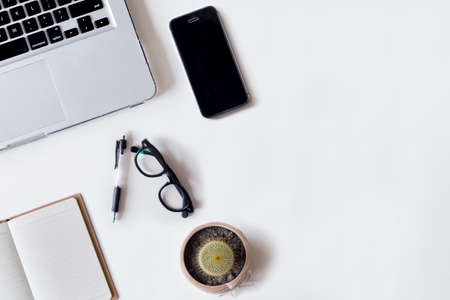 White office desk table with laptop, pen, smartphone, cactus, and notebook. Top view with copy space, flat lay.の写真素材