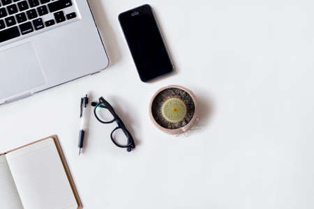 White office desk table with laptop, pen, smartphone, cactus, and notebook. Top view with copy space, flat lay.の写真素材