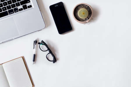 White office desk table with laptop, pen, smartphone, cactus, and notebook. Top view with copy space, flat lay.の写真素材