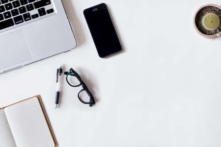 White office desk table with laptop, pen, smartphone, cactus, and notebook. Top view with copy space, flat lay.の写真素材
