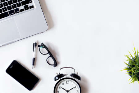 White office desk table with laptop, smartphone, alarm,plan and glass. Top view with copy space, flat lay.の写真素材