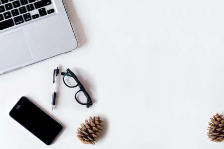 White office desk table with laptop, smartphone, pine cone and glass. Top view with copy space, flat lay.の写真素材