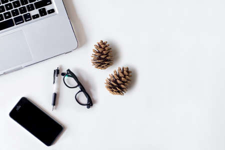 White office desk table with laptop, smartphone, pine cone and glass. Top view with copy space, flat lay.の写真素材