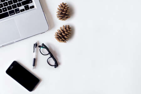 White office desk table with laptop, smartphone, pine cone and glass. Top view with copy space, flat lay.の写真素材