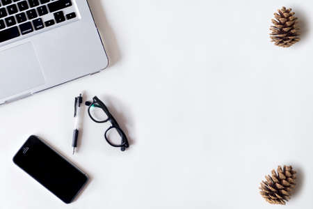 White office desk table with laptop, smartphone, pine cone and glass. Top view with copy space, flat lay.の写真素材