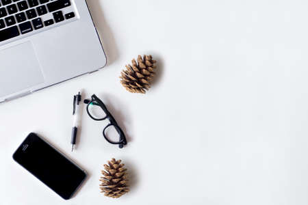 White office desk table with laptop, smartphone, pine cone and glass. Top view with copy space, flat lay.の写真素材