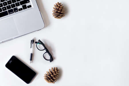 White office desk table with laptop, smartphone, pine cone and glass. Top view with copy space, flat lay.の写真素材