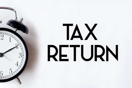 Tax return word written on white office desk table with alarm clock.の写真素材