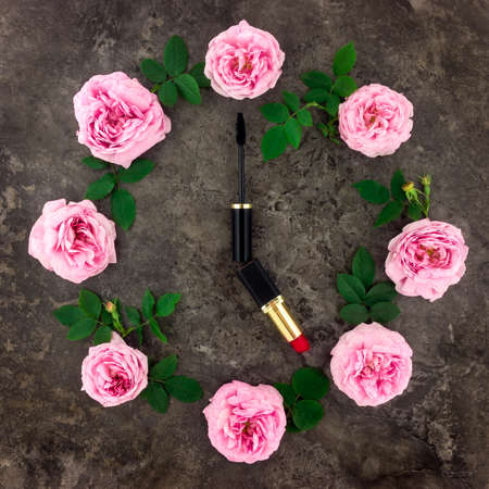 Decorative flat lay composition with cosmetics and flowers. Make up time concept. Top view on dark backgroundの写真素材