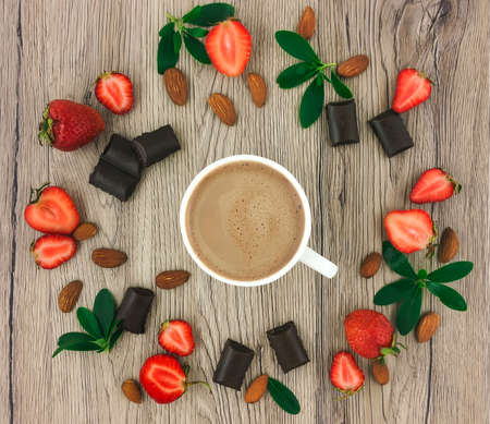 Cup of coffee with milk, chocolate, almonds and strawberries on wooden background. Flat lay, top viewの写真素材