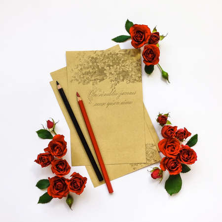 Decorative composition of empty old paper sheets with pencils and red roses on white background. Flat lay, top view, writing or painting conceptの写真素材