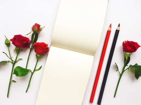 Colorful composition with sketchbook, red roses and pencils. Flat lay on white table, top view, overhead view with copy spaceの写真素材