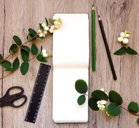 Closeup of notebook and stationery on wooden background, decorated with green snowberry branches....