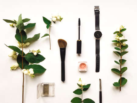 Colorful composition with woman watch, make up tools and accessories, decorated with green snowberry branches and berries. Flat lay on white table, top view, view from aboveの写真素材