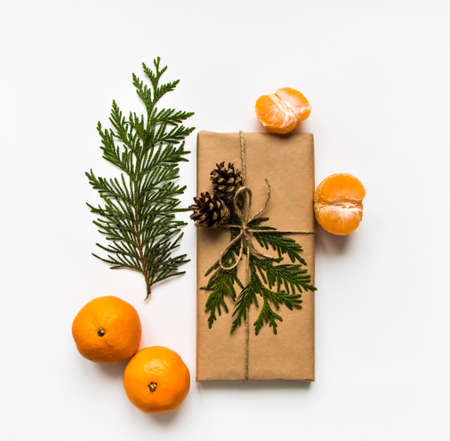 Vintage gift box in craft paper on white background. Present decorated with thuja branches, cones and tangerines. Christmas or other holiday concept, top view, flat layの写真素材